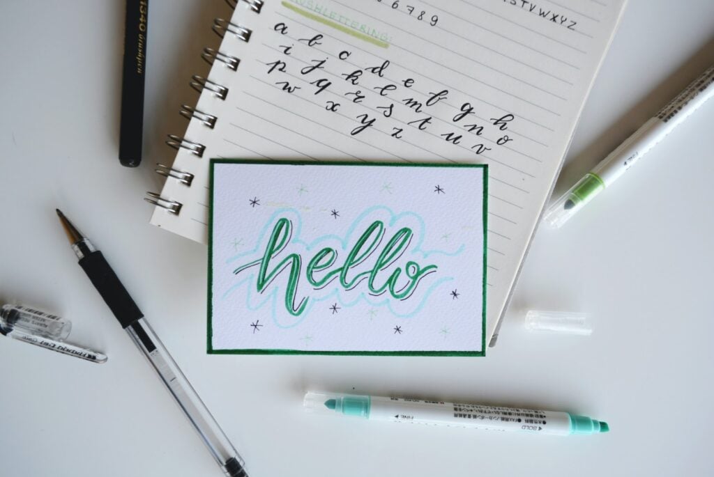 Calligraphy font drawn on a postcard laying on top of a wire-o booklet