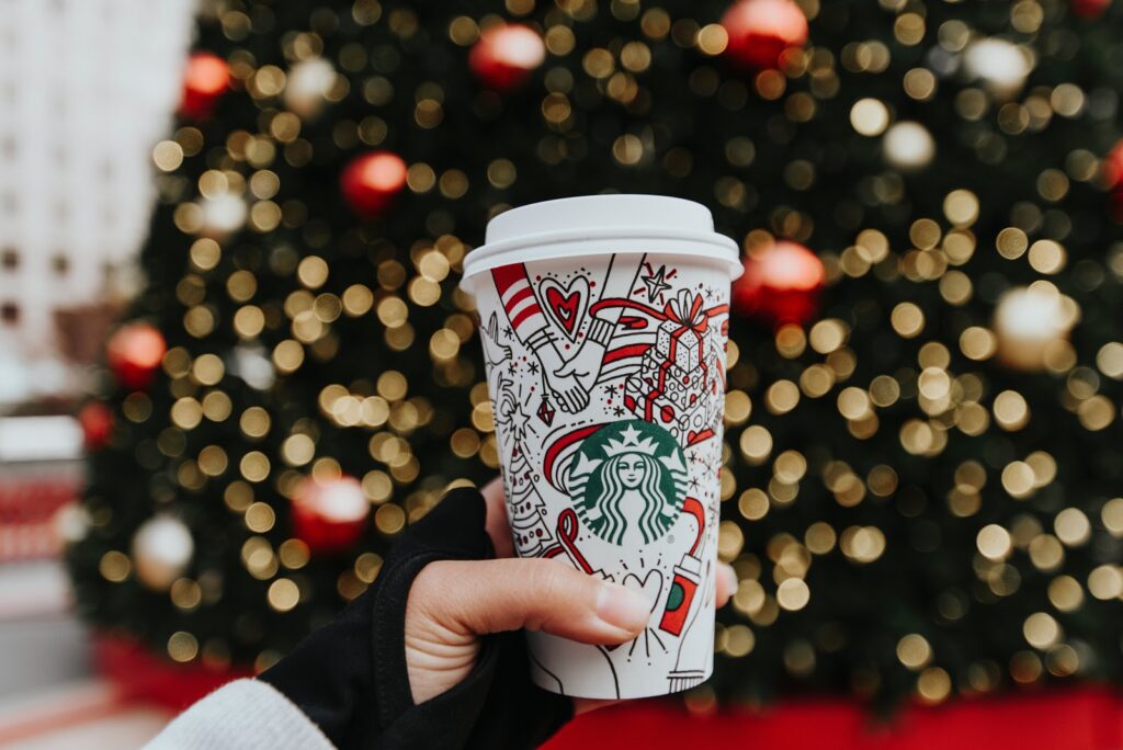 A hand holding a decorated coffee cup in front of a Christmas tree.