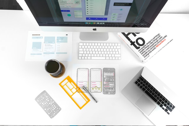 Desk with a computer, keyboard, laptop, and sketches