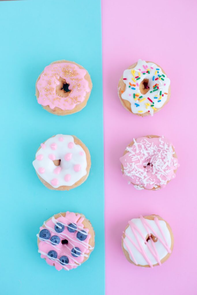 Donuts with different colored icing and sprinkles with a blue and pink background