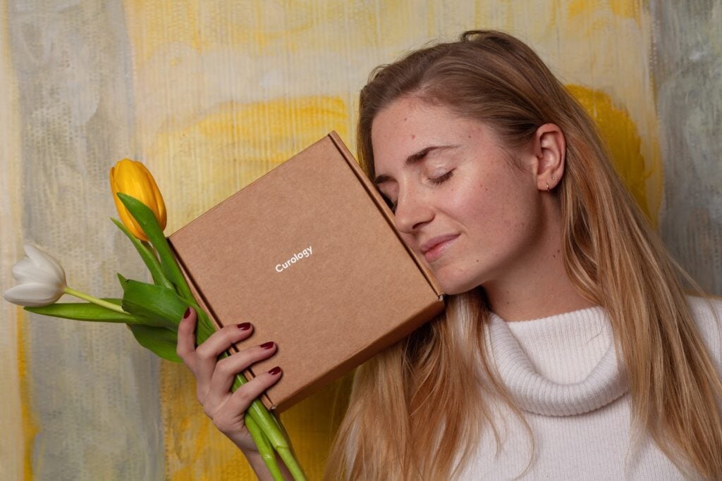 Whoman holding flowers and a custom shipping box next to her face